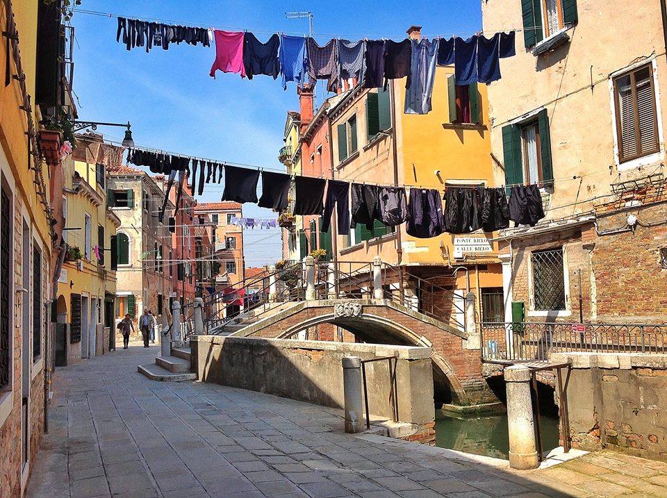 Calli veneziane con panni stesi e ponticello sul canale, simbolo autentico della vita quotidiana a Venezia.