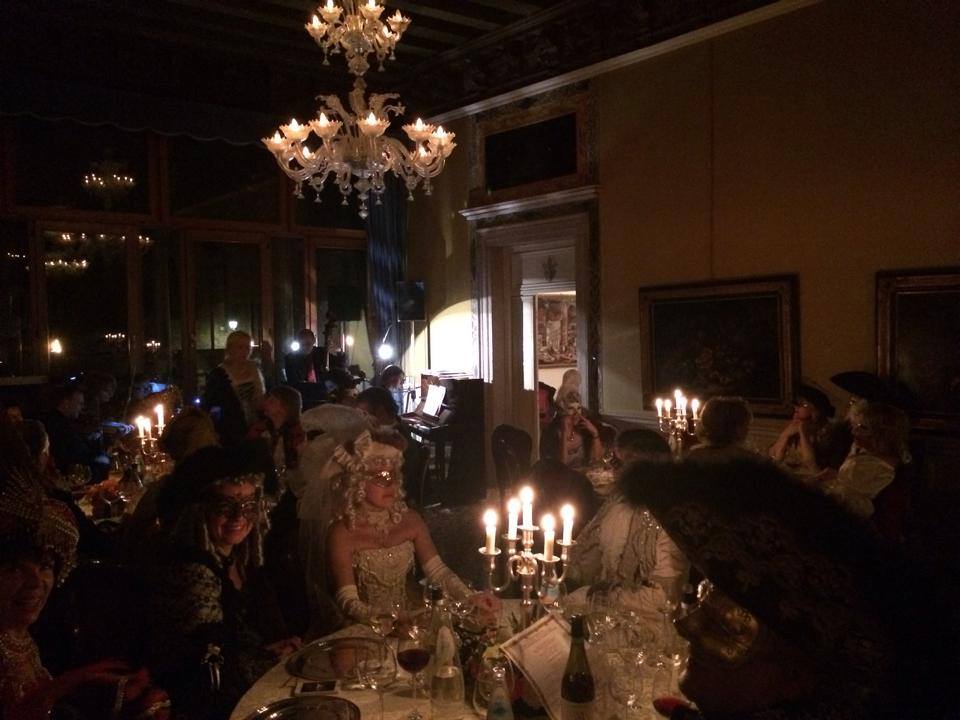 Balli privati e cena di gala in maschera a Venezia con ospiti in costumi d’epoca, luci soffuse e candelabri, atmosfera elegante in palazzo storico.