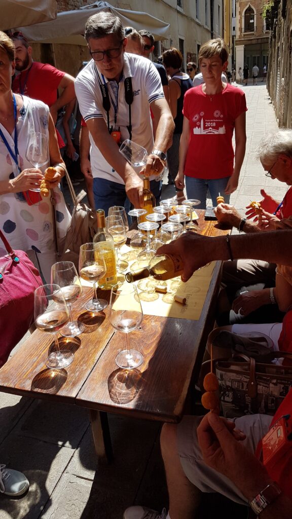 Partecipanti a un Bacaro Tour a Venezia degustano vini e cicchetti durante un’attività di team building.