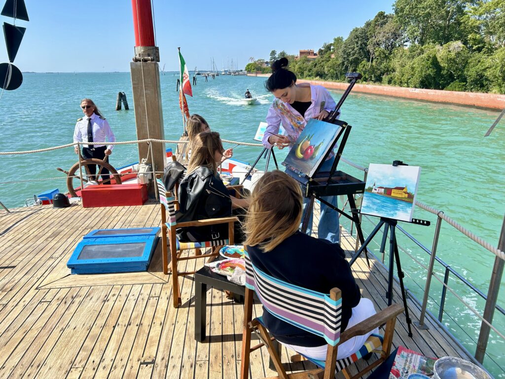 Corsi di pittura a Venezia durante un’attività di team building creativo in barca, con partecipanti che dipingono tele ispirati dalla laguna.