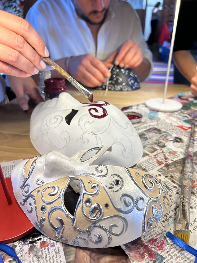 Laboratorio di Decorazione Maschere Veneziane durante un’attività di team building, con partecipanti che dipingono e decorano maschere in cartapesta con colori e dettagli artigianali.