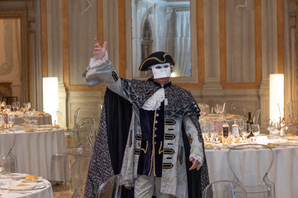 Attore in costume barocco e maschera bianca durante La Cena d’Artista a Venezia, evento di team building tra arte e cucina in palazzo storico.