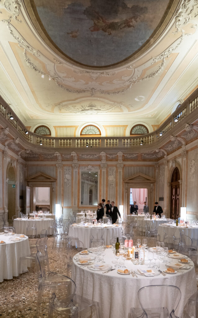 Sala storica a Venezia allestita per cena di gala con tavoli rotondi eleganti e decorazioni raffinate.