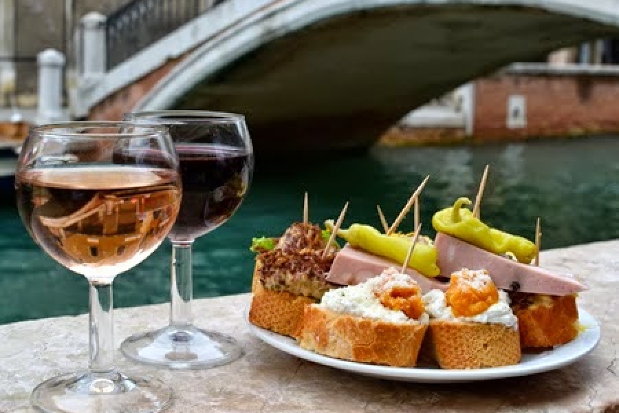Cicchetti veneziani e calici di vino davanti a un ponte sui canali di Venezia